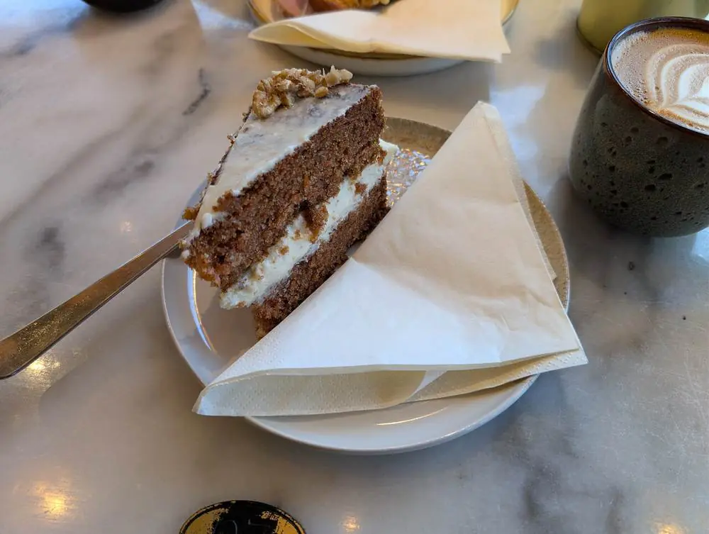 A tall carrot cake with cream cheese frosting on a cake stand