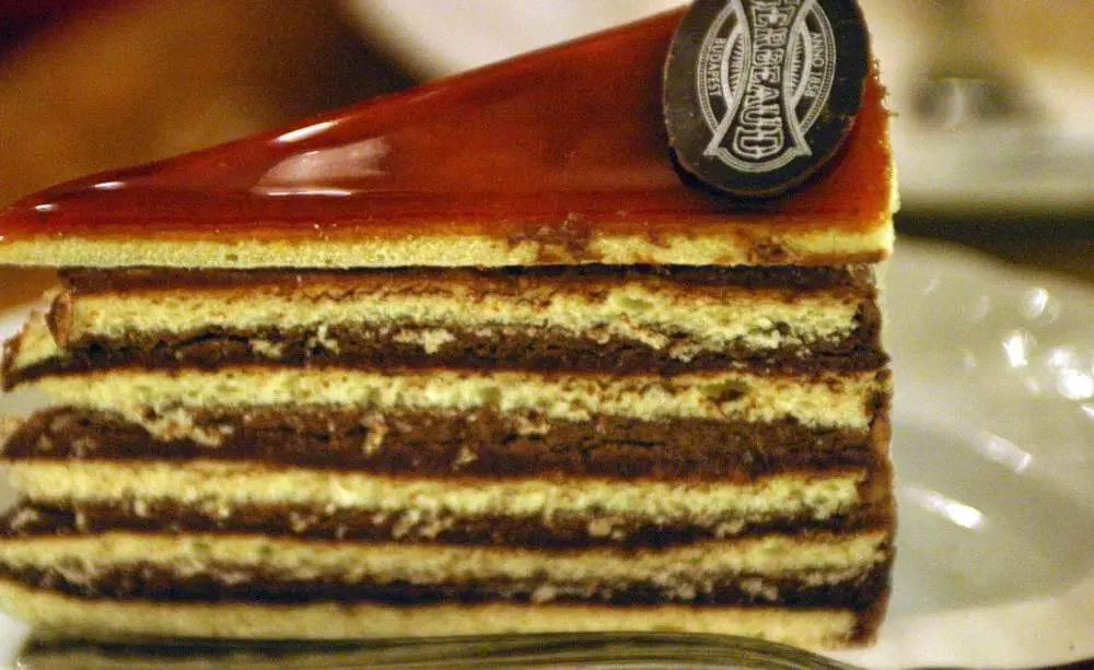 A slice of Dobos torte showing thin sponge layers, chocolate buttercream and a glossy caramel top